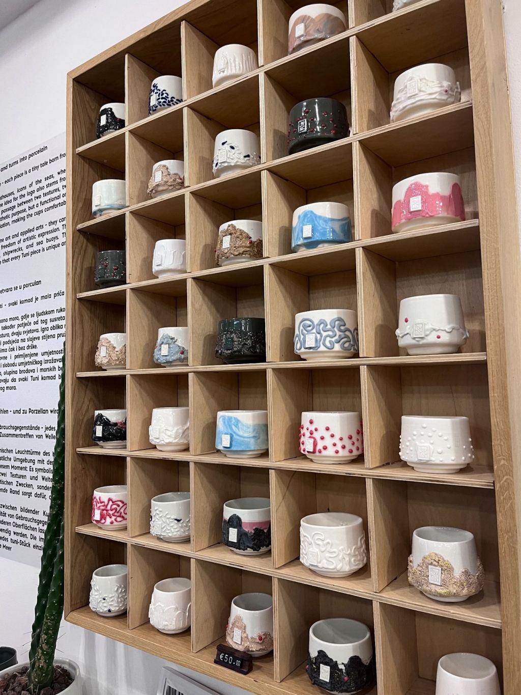 Wooden shelf with many compartments full of handmade porcelain cups in white, pink, blue and black