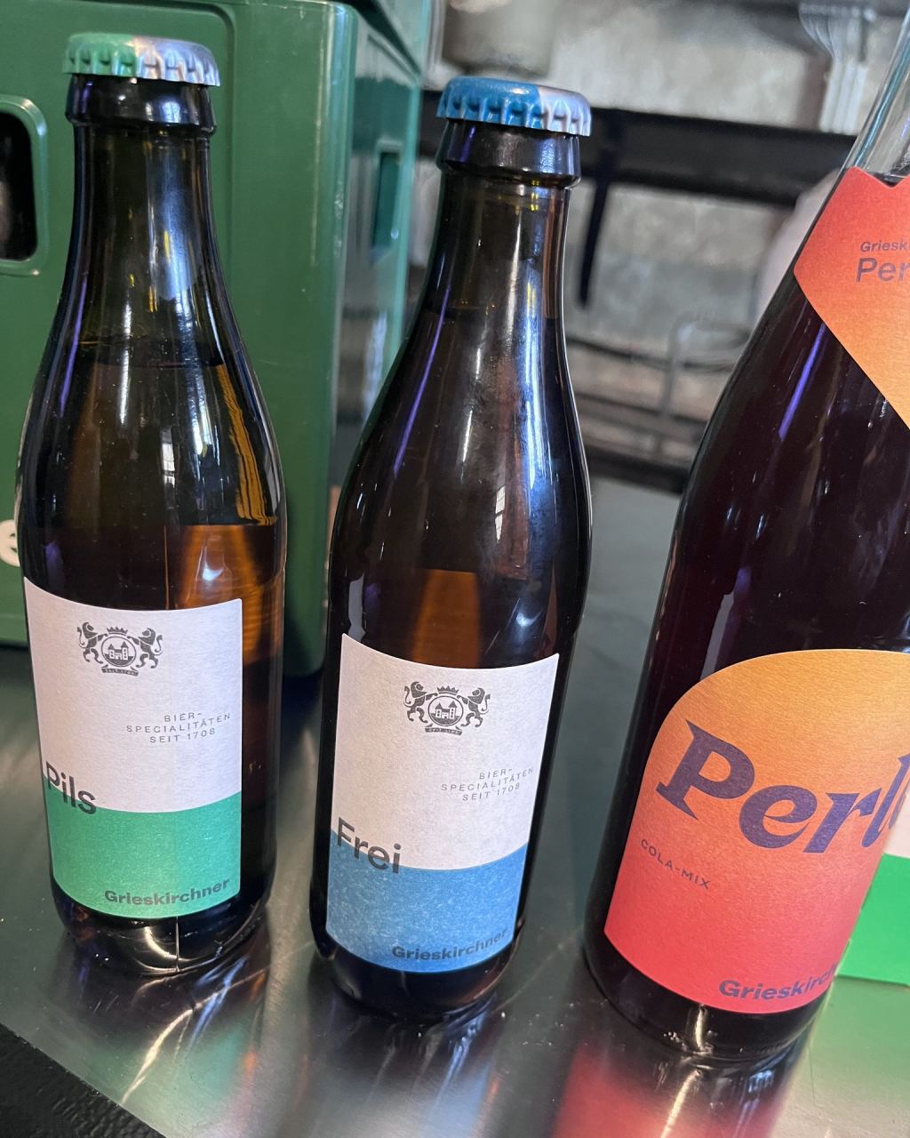 Drei Flaschen von Grieskirchner auf einer Theke: Pils, das alkoholfreie Frei und ein Cola-Mix