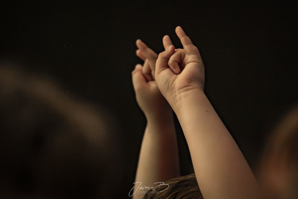 Zwei Kinderhände strecken sich vor dunklem Hintergrund in die Luft
