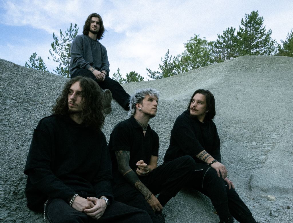 Die Band Baby Lasagna: vier Musiker in Schwarz sitzen auf grauem Fels vor Kiefern und Himmel, in der Mitte Marko Purišić mit silbergrauem Haar
