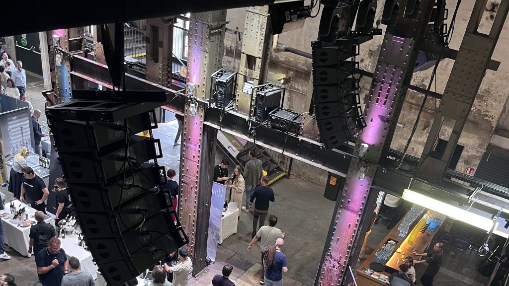 Blick von oben in eine Halle der Ottakringer Brauerei mit Lautsprechertürmen, Stahlträgern und Messeständen